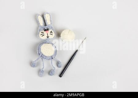 Knitted children's toy hare or bunny with a balls of thread and a crochet hook on a gray background. Stock Photo