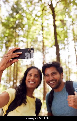 Couple Taking Selfie With Mobile Phone Hiking Or Walking Through Woodland Countryside Stock Photo