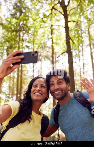 Couple Taking Selfie With Mobile Phone Hiking Or Walking Through Woodland Countryside Stock Photo
