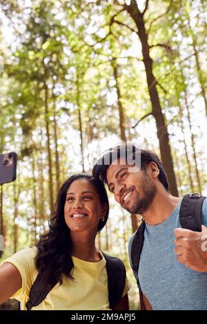 Couple Taking Selfie With Mobile Phone Hiking Or Walking Through Woodland Countryside Stock Photo