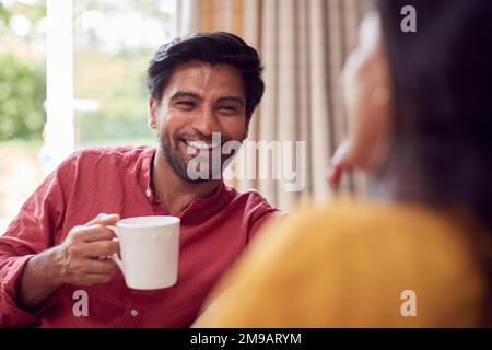 Couple Relaxing On Sofa At Home Together With Hot Drinks Stock Photo