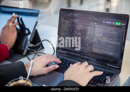 Female programmer writes some code and drinks coffee while sitting near her colleague Stock Photo