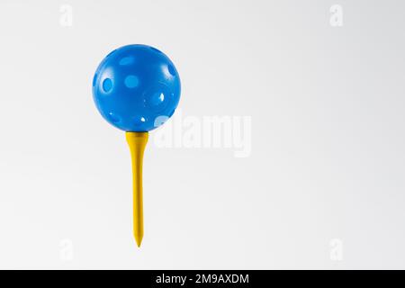 blue airflow perforated golf practice ball on a yellow tee   isolated on a white background Stock Photo