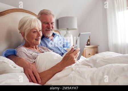 Retired Senior Couple In Bed At Home Using Digital Tablet Stock Photo