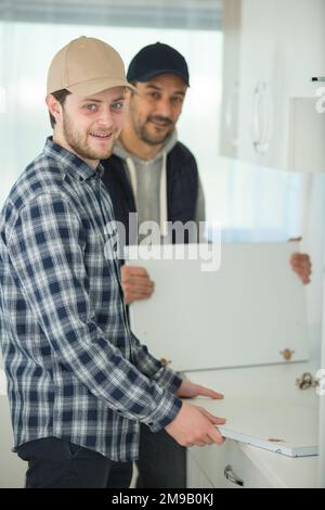 two handymen fixing sink door in kitchen Stock Photo