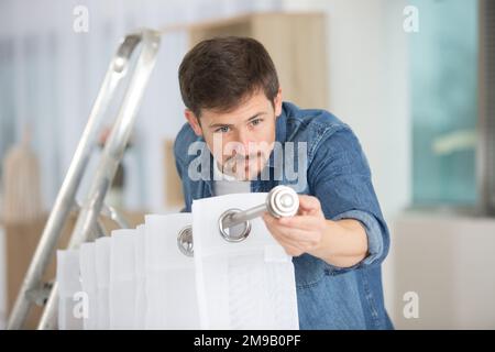 man hanging window curtain indoors Stock Photo