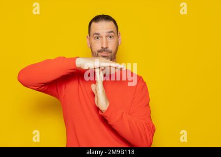 Latino man with a beard in a red sweatshirt making the time-out gesture, he needs a break from the pace of life demanded of middle-class people Stock Photo