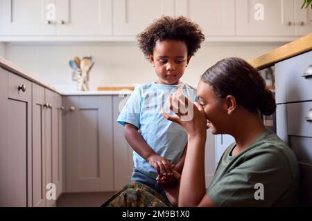 Young Son Comforting Depressed Mother In Uniform Suffering With PTSD Sitting On Floor On Home Leave Stock Photo