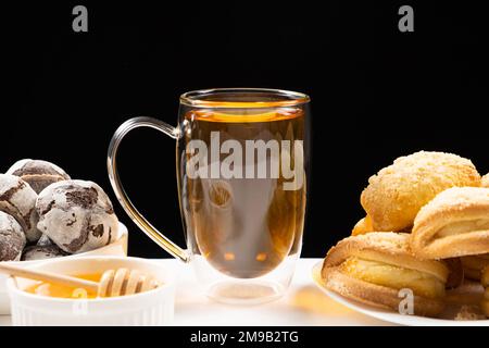Tea with honey with cocoa cookies and cakes with creamy filling on a black background. Stock Photo