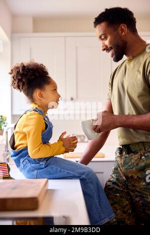 Daughter With American Army Father In Uniform On Home Leave Drinking Juice In Kitchen Stock Photo