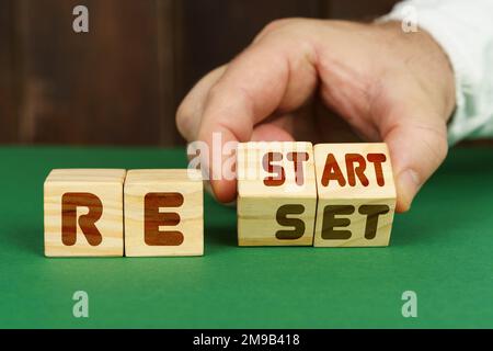 Technology concept. On a green surface, a man puts cubes with the inscription - RESTART, RESET Stock Photo