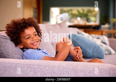 Portrait Of Smiling Boy Relaxing Sitting On Sofa At Home Stock Photo