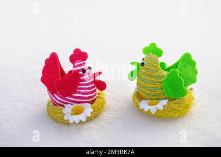 Figures of red and green twine chickens sitting on a nest. Easter symbols on the snow are a symbol of the spring holiday. Stock Photo