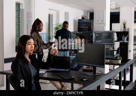 Asian web developer working with hologram and coding language in programming software company. Programmer analyzing holographic html code and augmented reality to develop new server interface. Stock Photo