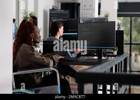 Wheelchair user typing script code on computer, working with cloud computing terminal window. Disabled web developer writing artificial intelligence algorithm in it big data company office. Stock Photo