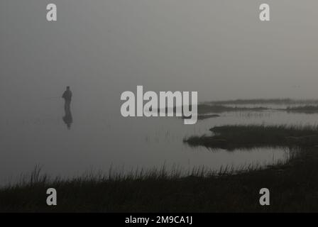 Lone angler fishing on a misty lake. Stock Photo