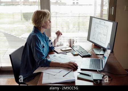 Focused mature woman engineer constructor works on project from home office using computer Stock Photo