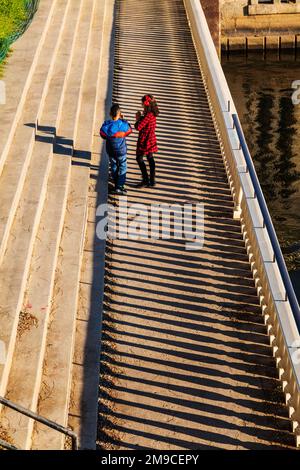 Young boy & girl skipping happily along sunlit stone path; Fairmount Water Works; Philadelphia; Pennsylvania; USA Stock Photo