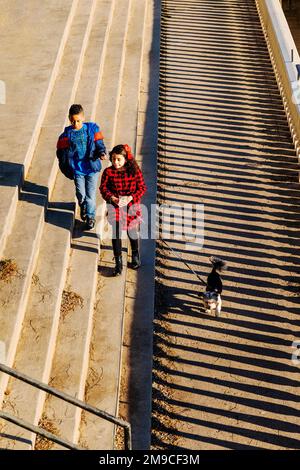 Young boy & girl with pet dog skipping happily along sunlit stone path; Fairmount Water Works; Philadelphia; Pennsylvania; USA Stock Photo