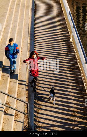 Young boy & girl with pet dog skipping happily along sunlit stone path; Fairmount Water Works; Philadelphia; Pennsylvania; USA Stock Photo