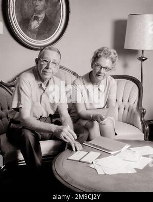 1970s SENIOR COUPLE MAN AND WOMAN SITTING AT COFFEE TABLE WITH CHECKBOOK PAYING BILLS LOOKING AT CAMERA - s18891 HAR001 HARS PAPERWORK FRIEND SECURITY TEAMWORK INFORMATION LIFESTYLE ELDER FEMALES MARRIED SPOUSE HUSBANDS GROWNUP HEALTHINESS HOME LIFE COPY SPACE FRIENDSHIP HALF-LENGTH LADIES PERSONS GROWN-UP CARING MALES RETIREMENT SERENITY CONFIDENCE SENIOR MAN PAYING SENIOR ADULT MIDDLE-AGED B&W PARTNER MIDDLE-AGED MAN EYE CONTACT SENIOR WOMAN GOALS HAPPINESS MIDDLE-AGED WOMAN OLDSTERS HIGH ANGLE OLDSTER ACCOUNTS ACCOUNT STRATEGY PAY CONNECTION REVIEWING ACCOUNTING BUDGETS FRIENDLY ELDERLY MAN Stock Photo