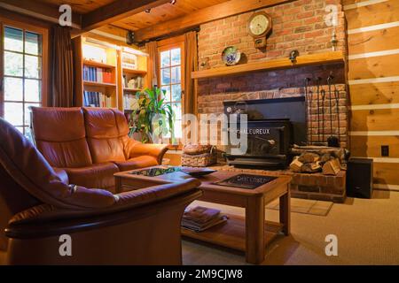 Brown leather sofas, wooden coffee table with glass tops in front of red brick wood burning stove in living room inside Canadiana style log home. Stock Photo