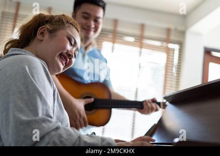 Young Asian chubby couple singing and playing acoustic guitar and piano together. Man and woman enjoying musical instrument. People in a band practicing in the house Stock Photo