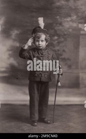 A delightful photograph of a young Edwardian boy in a sailor suit, raising his hand in a salute. Stock Photo