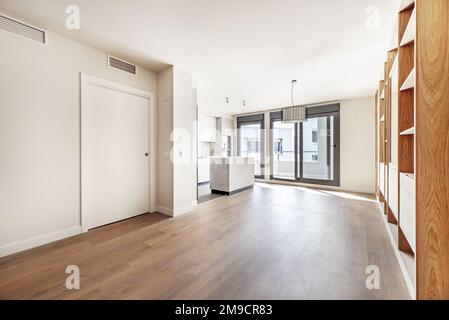 Apartment with a kitchen with smooth gray cabinets and an island open to the living room with a custom-made oak bookcase, large windows with sliding g Stock Photo