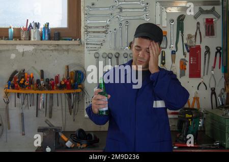 Image of a man in overalls holding a bottle of beer in his workshop. Break, relax after work. Stock Photo