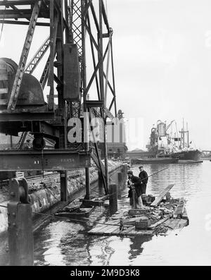 Dockside scene with men on a raft and vessels in the background, River Thames, Port of London. Stock Photo