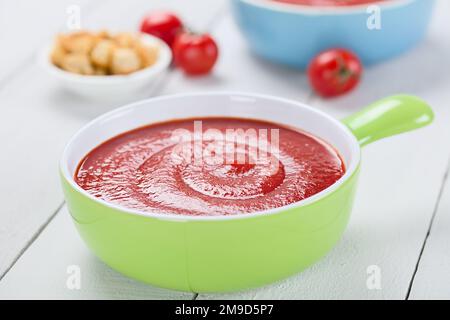 Fresh homemade tomato soup in colorful bowls, wholegrain croutons on the side, photographed on white wood (Selective Focus) Stock Photo