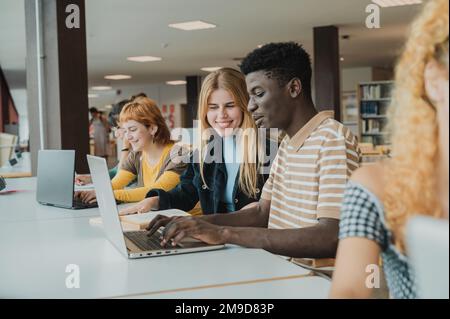 Cheerful diverse friends doing assignment using laptops in university Stock Photo