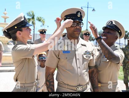 220517-N-OX321-1099 NAVAL AIR STATION SIGONELLA, Italy (May 17, 2022) – Senior Chief Master-at-Arms Laymoun Ferguson has his cover placed on by Naval Air Station Sigonella Command Master Chief Anna Wood, left, and his wife, Chief Personnel Specialist Naomie Ferguson, during a master chief and senior chief petty officer pinning ceremony on Naval Air Station Sigonella, May 17, 2022. NAS Sigonella’s strategic location enables U.S., allied, and partner nation forces to deploy and respond as required, ensuring security and stability in Europe, Africa and Central Command. Stock Photo