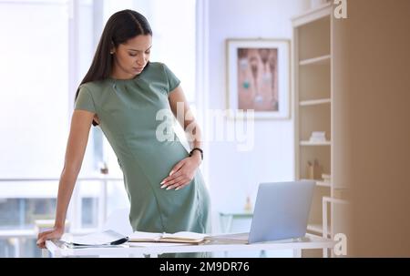 I think I need to see my doctor. a young pregnant businesswoman standing alone in the office and suffering from abdominal pain. Stock Photo
