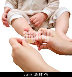 Mother woman sticks a medical band-aid on the toddler baby leg, isolated on a white background. Mom s hand with sticky wound protection tape and child Stock Photo