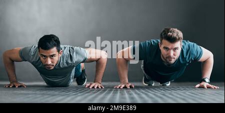 Working on their upper body. Full length portrait of two handsome young male athletes doing pushups side by side against a grey background. Stock Photo