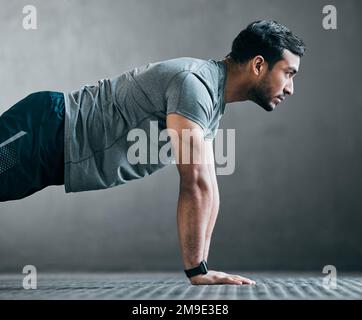 Rise and grind. a handsome young male athlete doing pushups against a grey background. Stock Photo