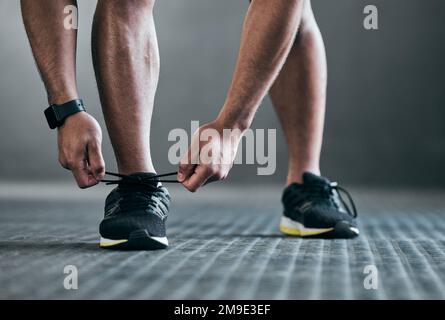 Ita all about preparation. an unrecognizable young male athlete tying his laces against a grey background. Stock Photo
