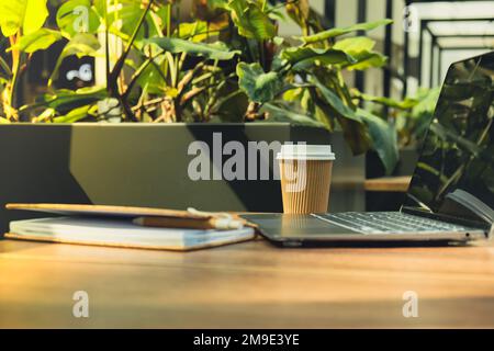 Mock up of modern laptop at table in co-working space. Remote Freelancer's place of work. Study and work online. Remote business education. Concept of webinar. E-learning Workstation Take away recycling coffee from paper cup. Coffee break Technology in Life Copy space Stock Photo