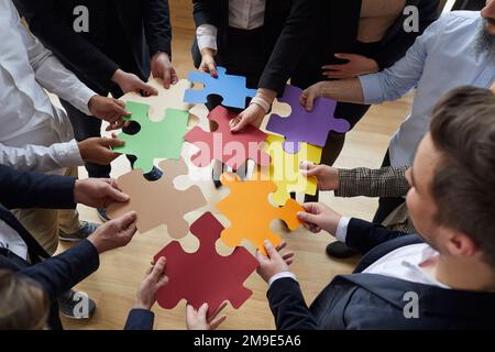 Pieces of colored puzzles in hands of people standing in circle and assembling them. Stock Photo