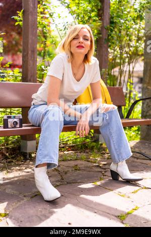 Blonde tourist girl on summer vacation sitting on a bench in a park Stock Photo