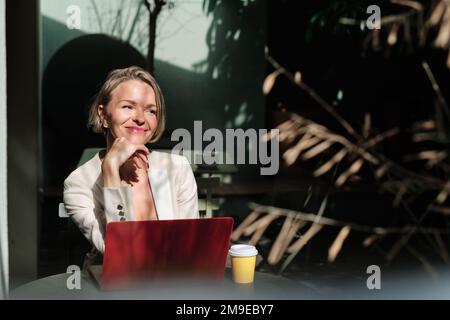 Relaxed businesswoman working with laptop while sitting outdoors in a cafe. Stock Photo