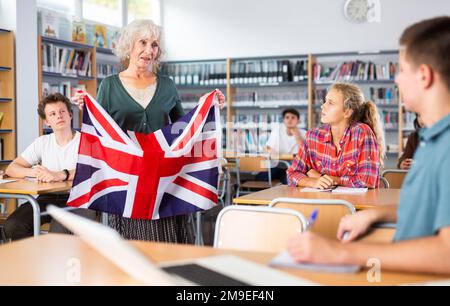 Elderly teacher shows the flag of Great Britain to teenagers and talks about this country during lesson at library school Stock Photo