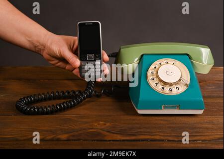 an old push-button mobile phone in a woman's hand next to an old vintage dial phone. Stock Photo