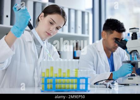 Going about a new test. a young woman using a dropper and test tube while working with samples in a lab alongside a colleague. Stock Photo