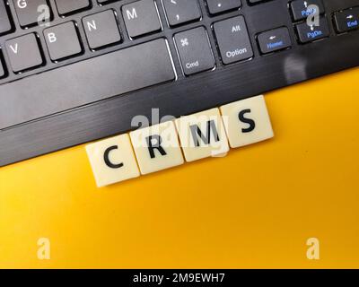 Black keyboard and toys word with the word CRMS on yellow background. Stock Photo