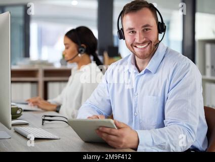 How can I make things better for you. a young man using a headset and digital tablet in a modern office. Stock Photo