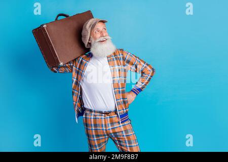 Photo of positive dreamy man pensioner wear checkered costume rising baggage looking empty space isolated blue color background Stock Photo
