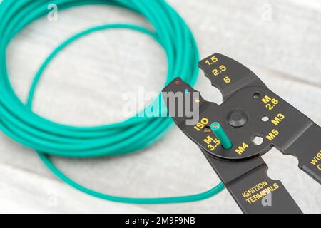 Close shot of Chinese made unbranded wire stripper & wire cutter for 26-10AWG wire (see Notes) with coiled role of green silicone covered wire. Stock Photo